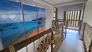 A corridor with a wooden railing and a view of a beach with boats.