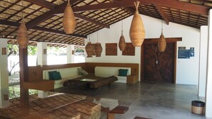 A spacious room with a high ceiling, wooden beams, a large table, a sofa set, and hanging woven light fixtures.