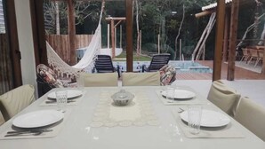 A dining area with a table set for four, a hammock, and a view of a pool and trees.