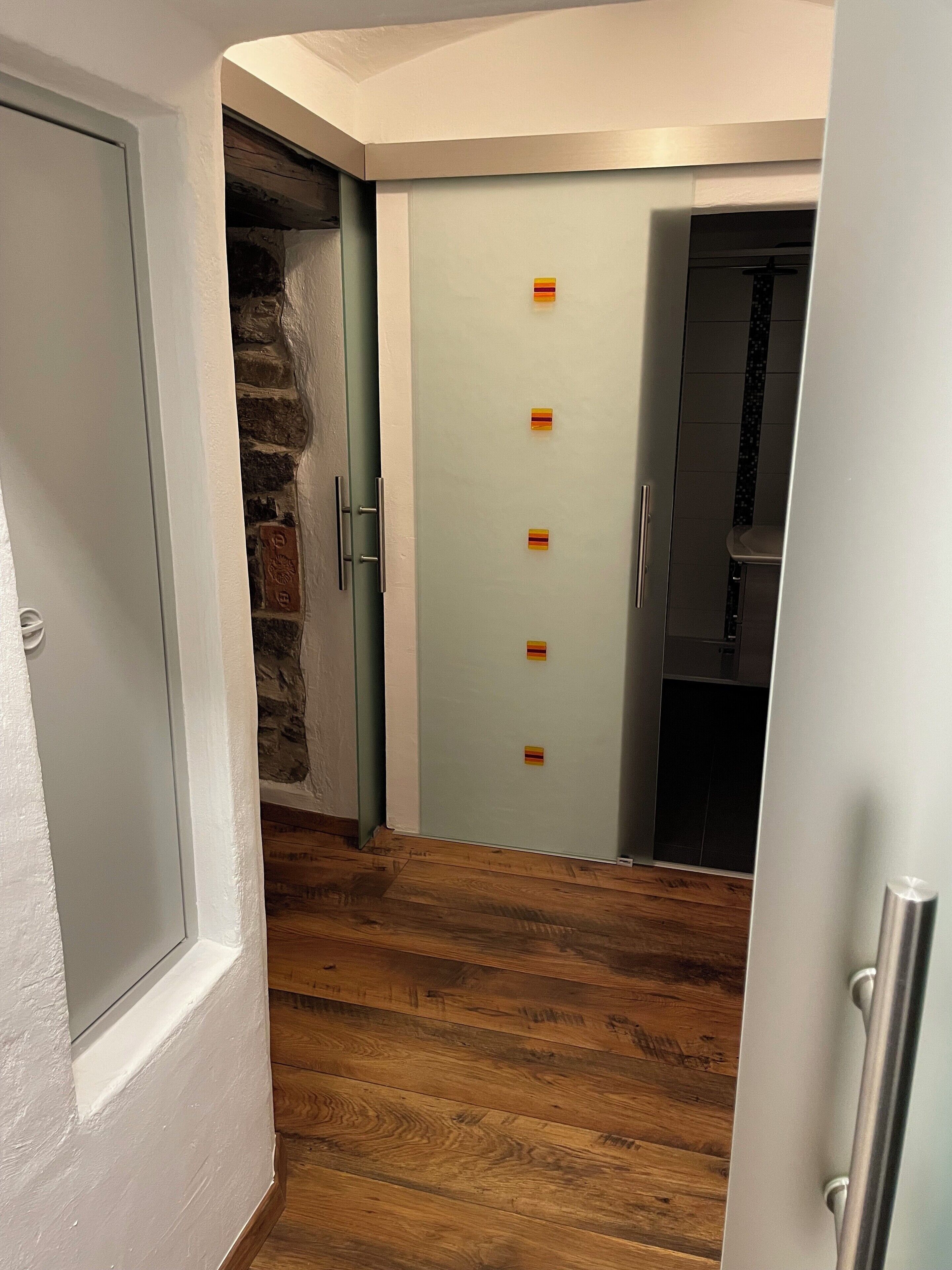 A hallway with a stone wall, a door with a light switch, and a wooden floor.