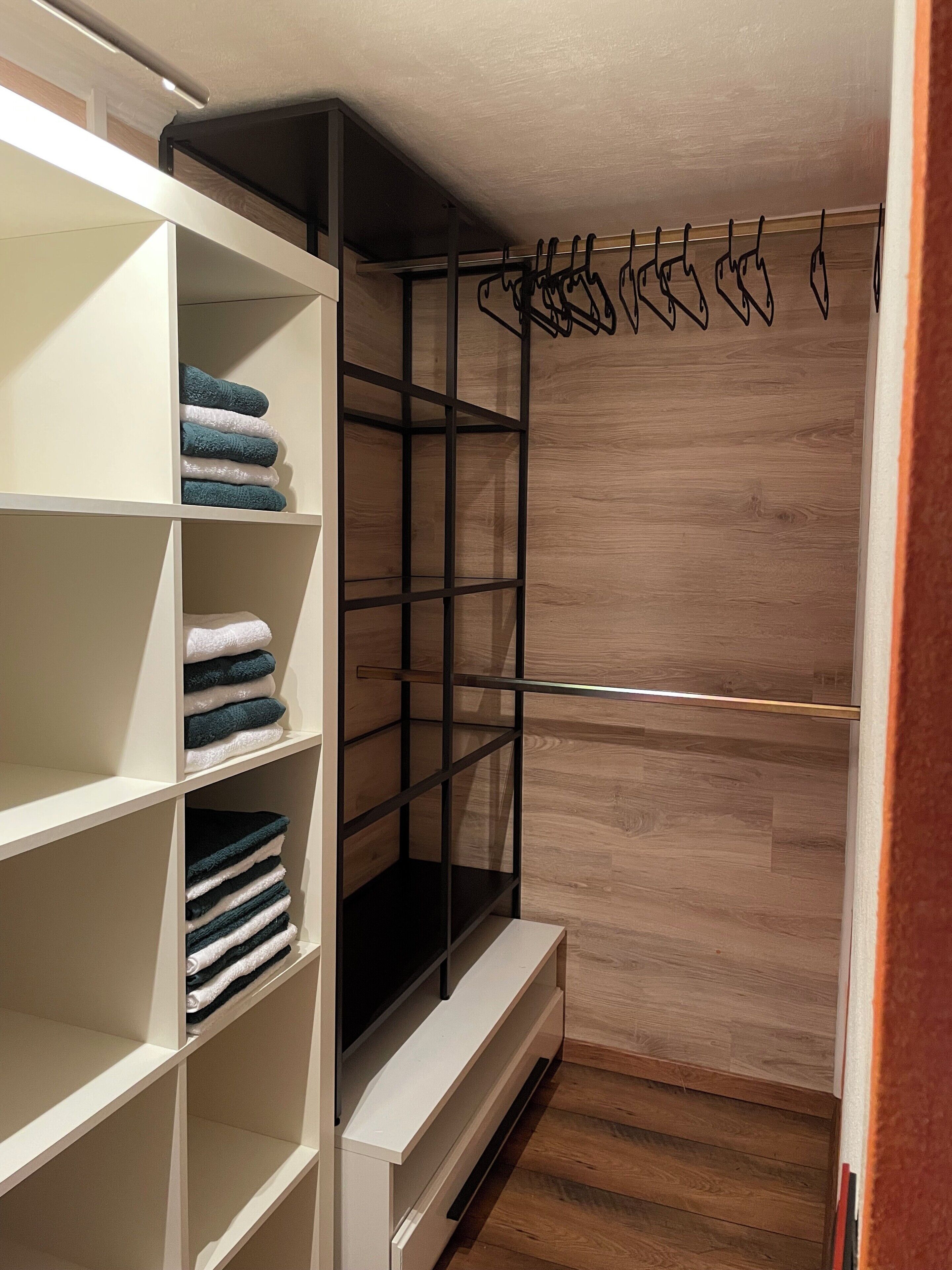 Un dressing avec des étagères blanches, une tringle noire et un plancher en bois.