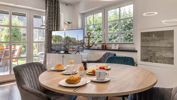 A modern dining area with a round table, chairs, and a television displaying a scenic view. - Apartment 50091 - Completely balanced: The first floor apartment is located in (Wittmund)