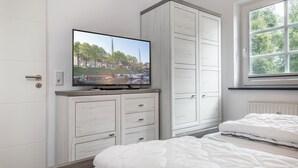 A bedroom with a bed, a television mounted on a cabinet, and a window with a view of trees. - Apartment 50091 - Completely balanced: The first floor apartment is located in (Wittmund)
