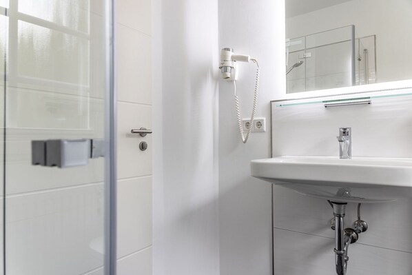 A modern bathroom with a glass shower enclosure, a white sink with a chrome faucet, and a mirror above the sink.