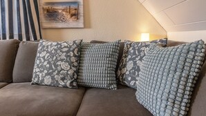 Un canapé marron agrémenté de coussins à motifs et un tableau sur le thème de la plage accroché au mur.