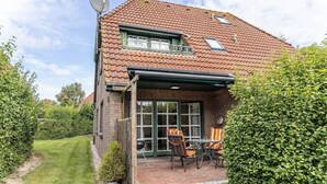 Une maison avec un toit en tuiles, un patio couvert avec des meubles d’extérieur et une antenne parabolique.