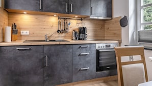 Une cuisine moderne avec des meubles de couleur sombre, un plan de travail en bois, un four Bosch et une fenêtre équipée de stores.