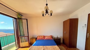 Un dormitorio con cama, mesita de noche, armario y vista al mar a través de una puerta corrediza.