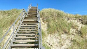 A wooden staircase leading up a sandy dune with grass on either side, under a clear blue sky. - Haus Sylter Schönheit - Welcome to Sylter Schönheit. (Sylt Westerland)
