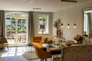 A dining area with a table set for four, a sofa, and a view of the outdoors through large windows.
