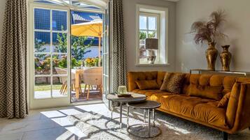 A living room with a sofa, a round coffee table, and a view of a garden through a glass door.