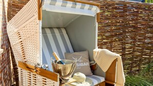 A wicker lounge chair with a striped cushion, a bottle of champagne, and a cushion with 'SIBAR' text. - Haus Sylter Schönheit - Welcome to Sylter Schönheit. (Sylt Westerland)