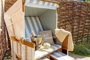 A wicker lounge chair with a striped cushion, a bottle of champagne, and a cushion with 'SIBAR' text. - Haus Sylter Schönheit - Sylter Schönheit - Exclusive comfort in a prime location (Sylt Westerland)