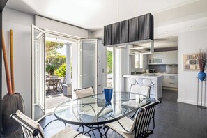 A modern kitchen with a central island, a glass dining table, and a view of the outdoors.