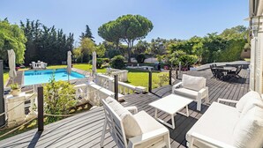A wooden deck with outdoor furniture, a swimming pool, and a large tree.
