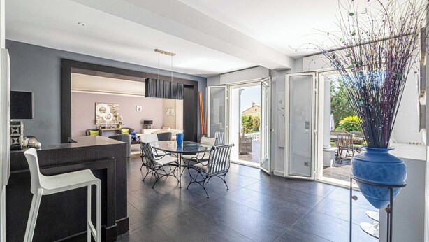 A modern kitchen with a dining area, a bar counter, and a large window.