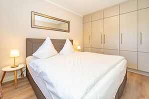 A hotel room with a large bed, two bedside lamps, a wardrobe, and a mirror on the wall. - Sünhair - NEW! Comfortable vacation apartment with balcony and modern furnishings in (Sylt)