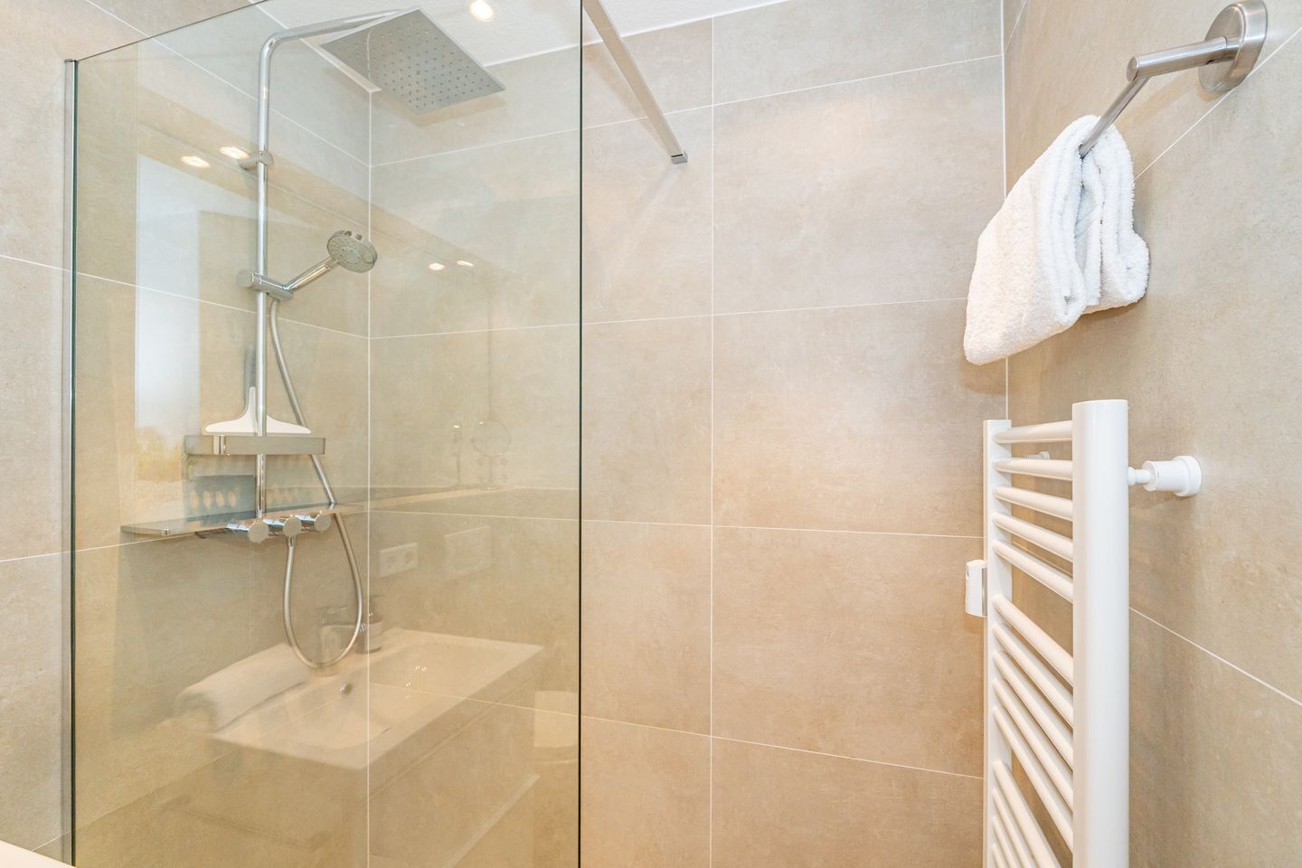 Ein modernes Badezimmer mit einer gläsernen Duschkabine, einem weißen Handtuchhalter und einem gefliesten Boden.