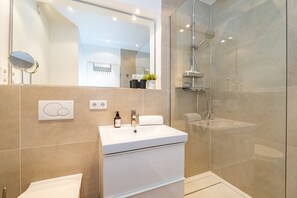 A modern bathroom with a white sink, mirror, and glass shower enclosure. - Sünhair - NEW! Comfortable vacation apartment with balcony and modern furnishings in (Sylt)