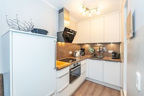 A compact kitchen with white cabinets, a wooden countertop, a built-in oven, and a coffee maker. - Sünhair - NEW! Comfortable vacation apartment with balcony and modern furnishings in (Sylt)