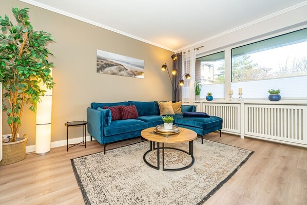 Un salon moderne avec un canapé bleu, une table basse ronde et une grande fenêtre avec des rideaux.