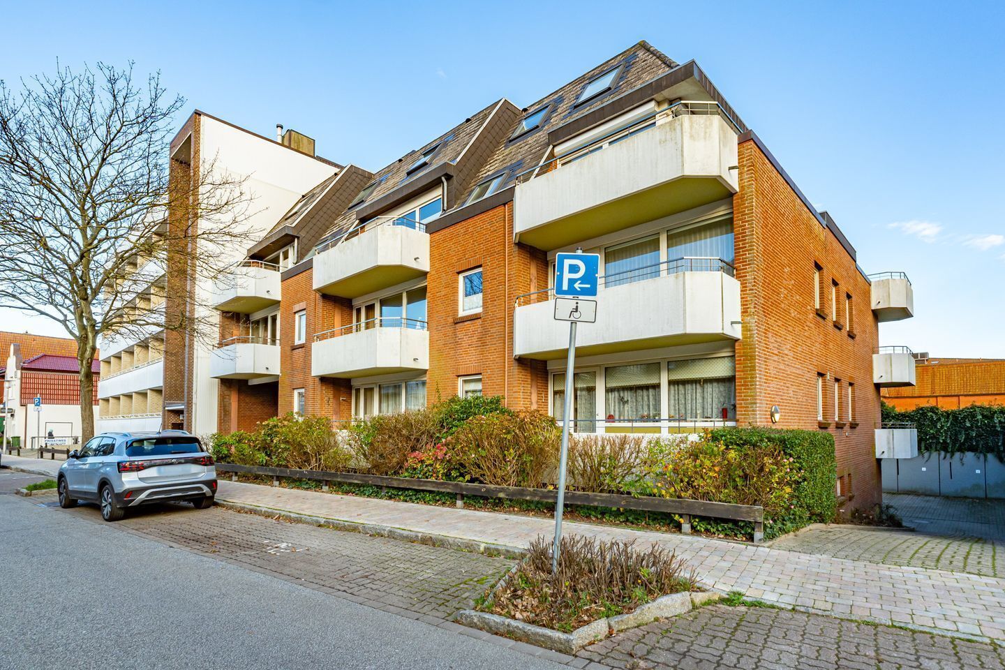 A multi-story residential building with a parking sign, a car parked in front, and a clear sky.
