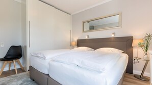 A double bed with a headboard, bedside lamps, a chair, and a mirror on the wall.