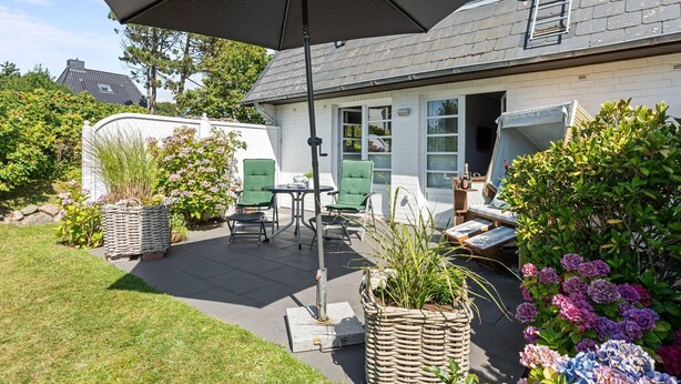 A patio area with outdoor furniture, a table, and a large umbrella providing shade.