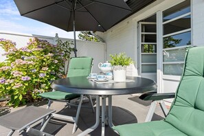 An outdoor patio with a round table, two chairs, an umbrella, and a potted plant.