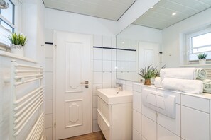 A modern bathroom with a white color scheme, a radiator, a sink, a mirror, and a window.