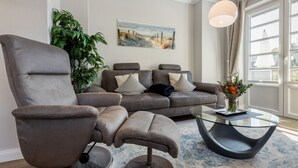 A modern living room with a grey sofa set, a glass coffee table, and a large window with curtains.