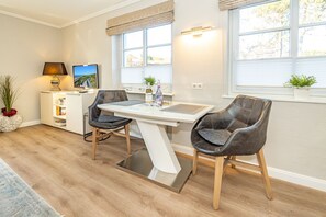 A modern kitchen with a dining table, two chairs, a TV, and a bookshelf.