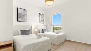 A modern hotel room with two beds, a wooden nightstand, a bedside table with a lamp, and a window with a view of the outside.