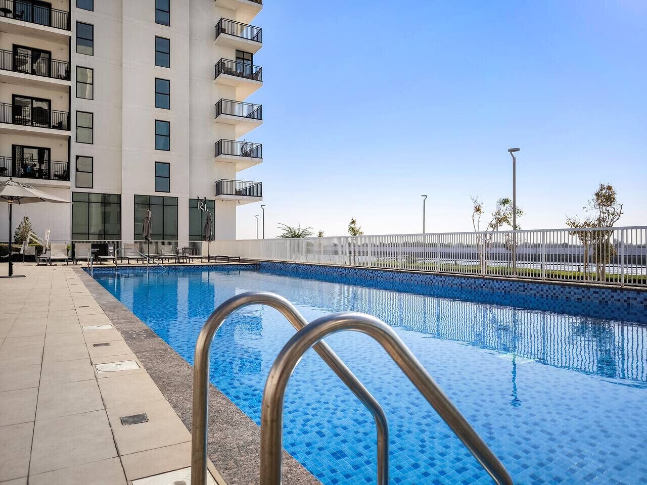 A swimming pool with metal railings, adjacent to a multi-story building with balconies.