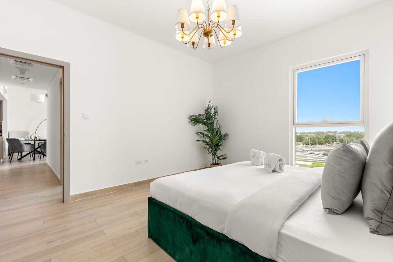 A modern bedroom with a large bed, a view of the city, and a dining area in the background.