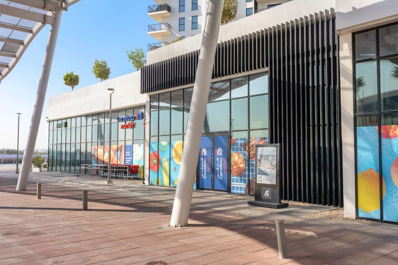 Een modern gebouw met grote glasramen, een metalen constructie links en een reeks kleurrijke fruitadvertenties rechts.
