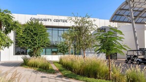 A modern building labeled "COMMUNITY CENTER" with a paved entrance, surrounded by greenery and a golf cart.