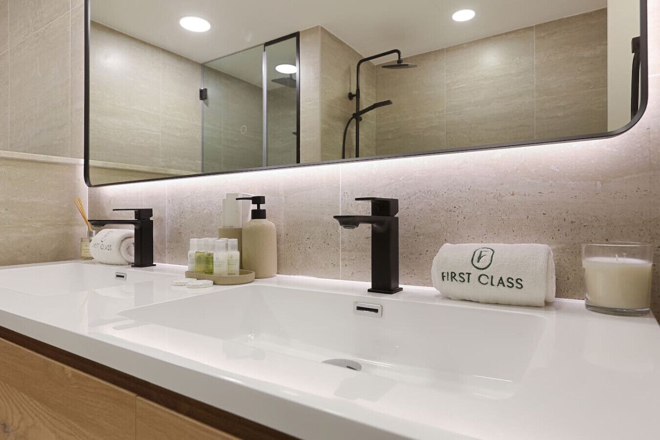 Un baño moderno con un espejo grande, dos lavamanos y un perchero con la etiqueta 'FIRST CLASS'.