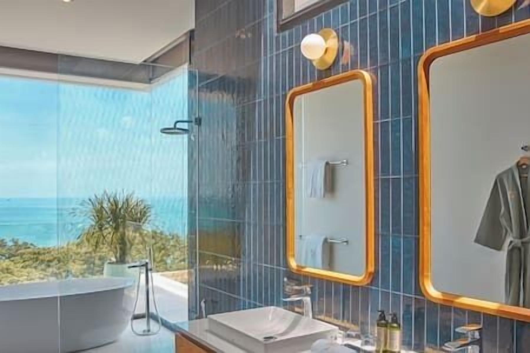 A modern bathroom with a large mirror, a bathtub, and a view of the ocean.