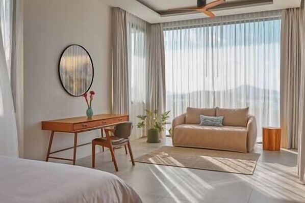 A modern hotel room with a bed, a desk, a sofa, and a large window with curtains.