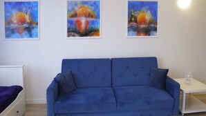 Une pièce avec un canapé bleu, une table de chevet blanche et trois tableaux encadrés accrochés au mur.