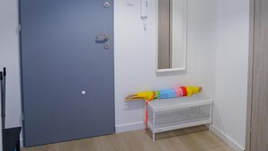Une pièce avec une porte bleue fermée, un téléphone blanc fixé au mur, une petite étagère blanche et un parapluie coloré posé sur l’étagère.