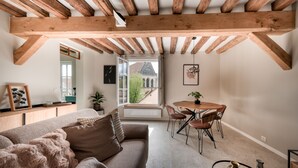 A cozy living room with a wooden ceiling, a sofa, a dining table with chairs, and a window with a view of a building. - The splendid Collégiale Saint André (Chartres)