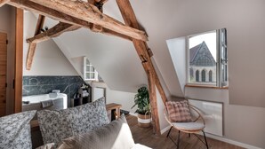 A cozy attic bedroom with exposed wooden beams, a view of a church steeple, a modern bathroom with a marble wall, and a comfortable seating area with a plant and a fluffy pillow. - The splendid Collégiale Saint André (Chartres)