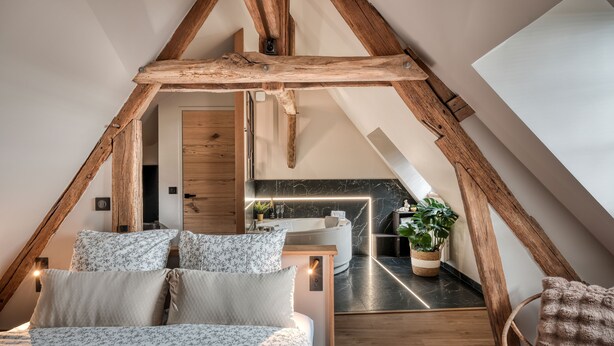 A cozy attic bedroom with a wooden ceiling, a bed with floral bedding, a small desk, and a potted plant. - The splendid Collégiale Saint André (Chartres)