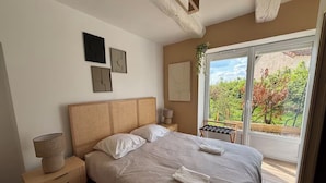 Un dormitorio con una cama grande, una mesita de noche, una lámpara y vistas al exterior a través de una puerta corrediza de vidrio.