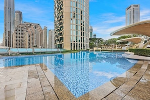 A swimming pool with a tiled edge, surrounded by a paved area and tall residential buildings in the background.