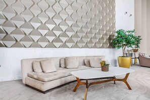 A modern living room with a beige sectional sofa, a white coffee table, and a decorative wall panel.