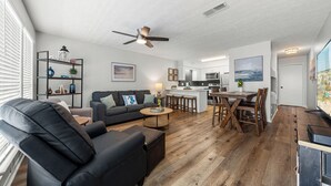 A modern living room with a black leather sofa, a wooden coffee table, and a ceiling fan. - Laguna Beach Community | Steps to Beach • Shared Pool + Pickleball | Gulf Walk (Panama City Beach)