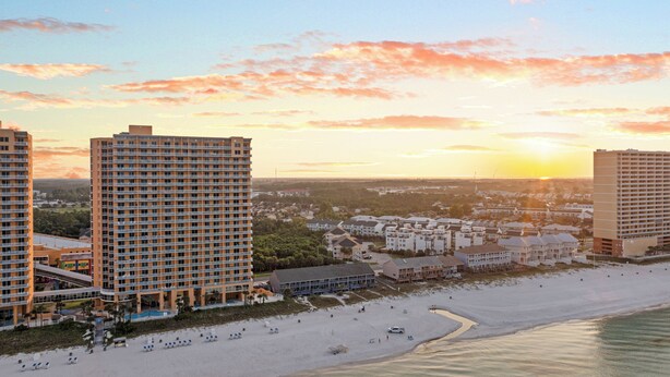 A beachfront hotel with multiple high-rise buildings, a sandy beach, and a clear view of the sunset. - Laguna Beach Community | Steps to Beach • Shared Pool + Pickleball | Gulf Walk (Panama City Beach)